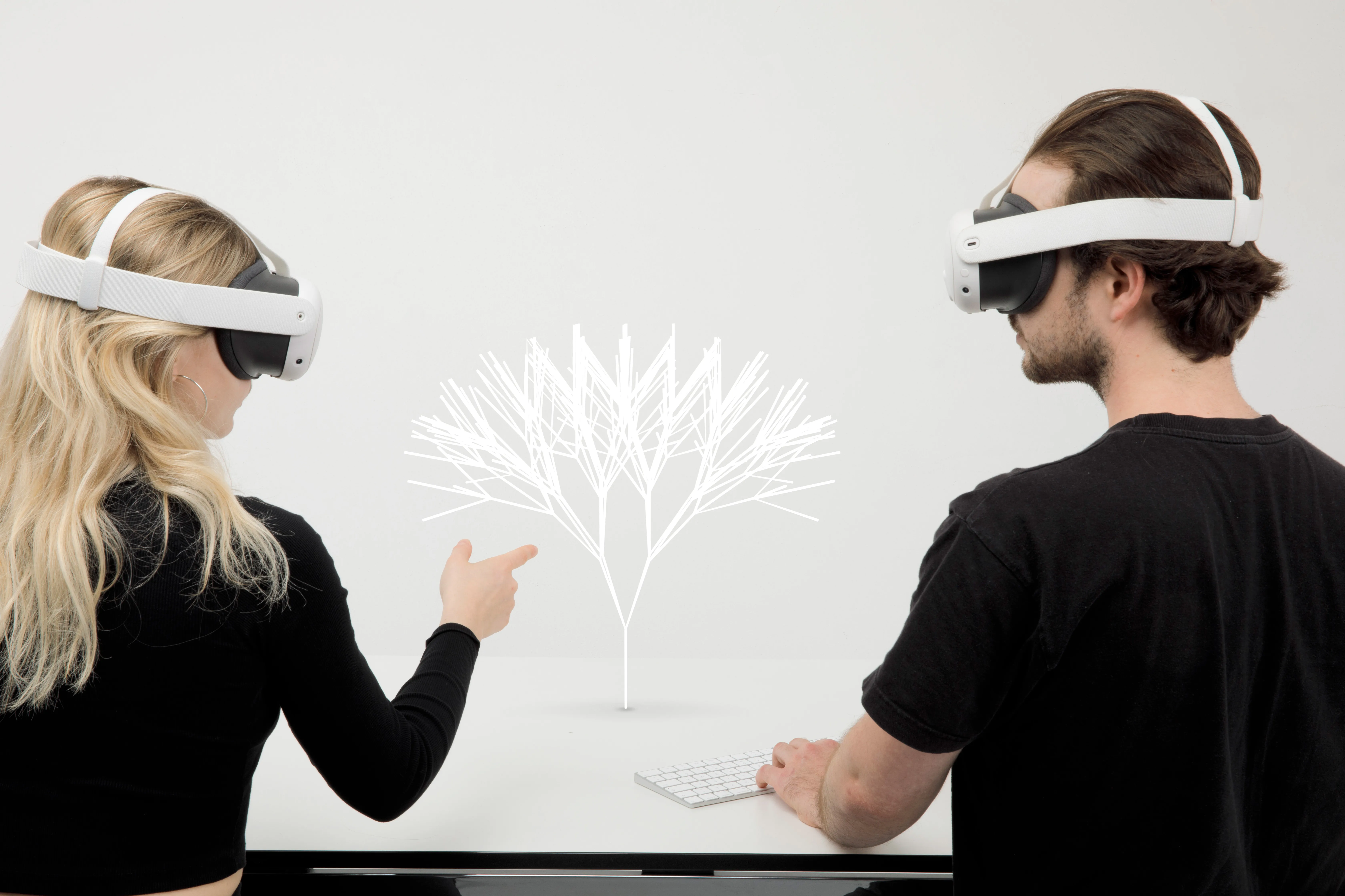 A blonde woman and brunette man looking at a minimal digital tree on a table through white mixed reality headsets.