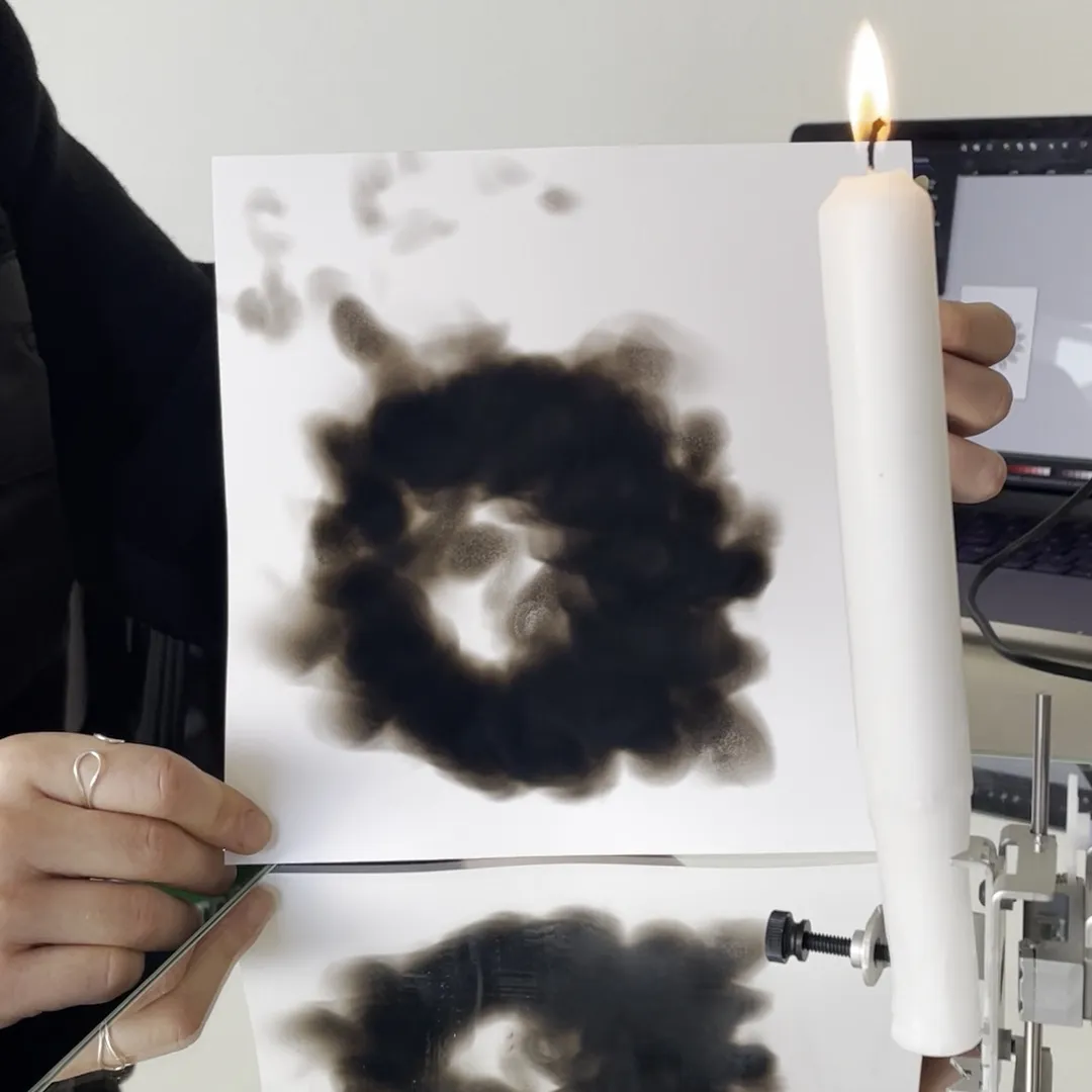 A white paper with circular burn marks next to a lit candle.