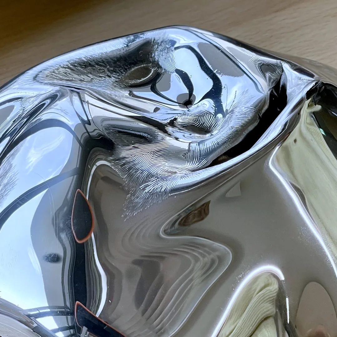 Close-up view of a crumpled and dented bowl with distorted reflections of its surroundings on a wooden surface.