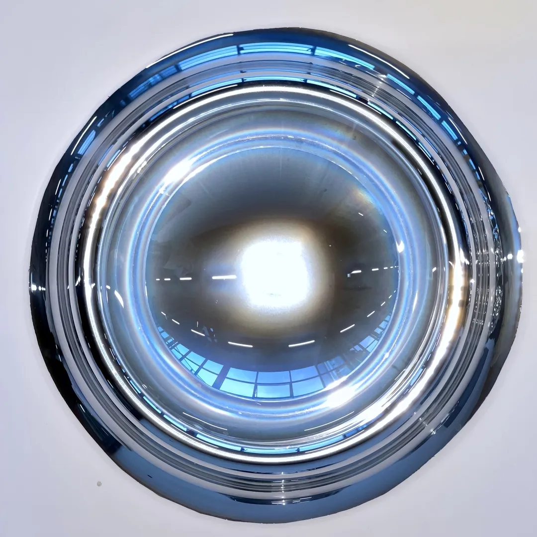 Top-down view of a reflective metallic bowl capturing bright lighting and distorted reflections of windows and its surroundings.